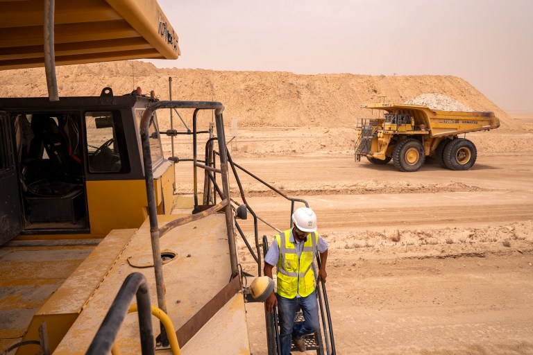 industrial mining image of worker climbing down from their dumbstruck and another drives by
